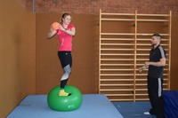 Wasserspringerin steht auf Gymnastikball und hält kleineren Ball in der Hand